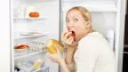 Donna davanti al frigo che si abbuffa per un attacco di fame